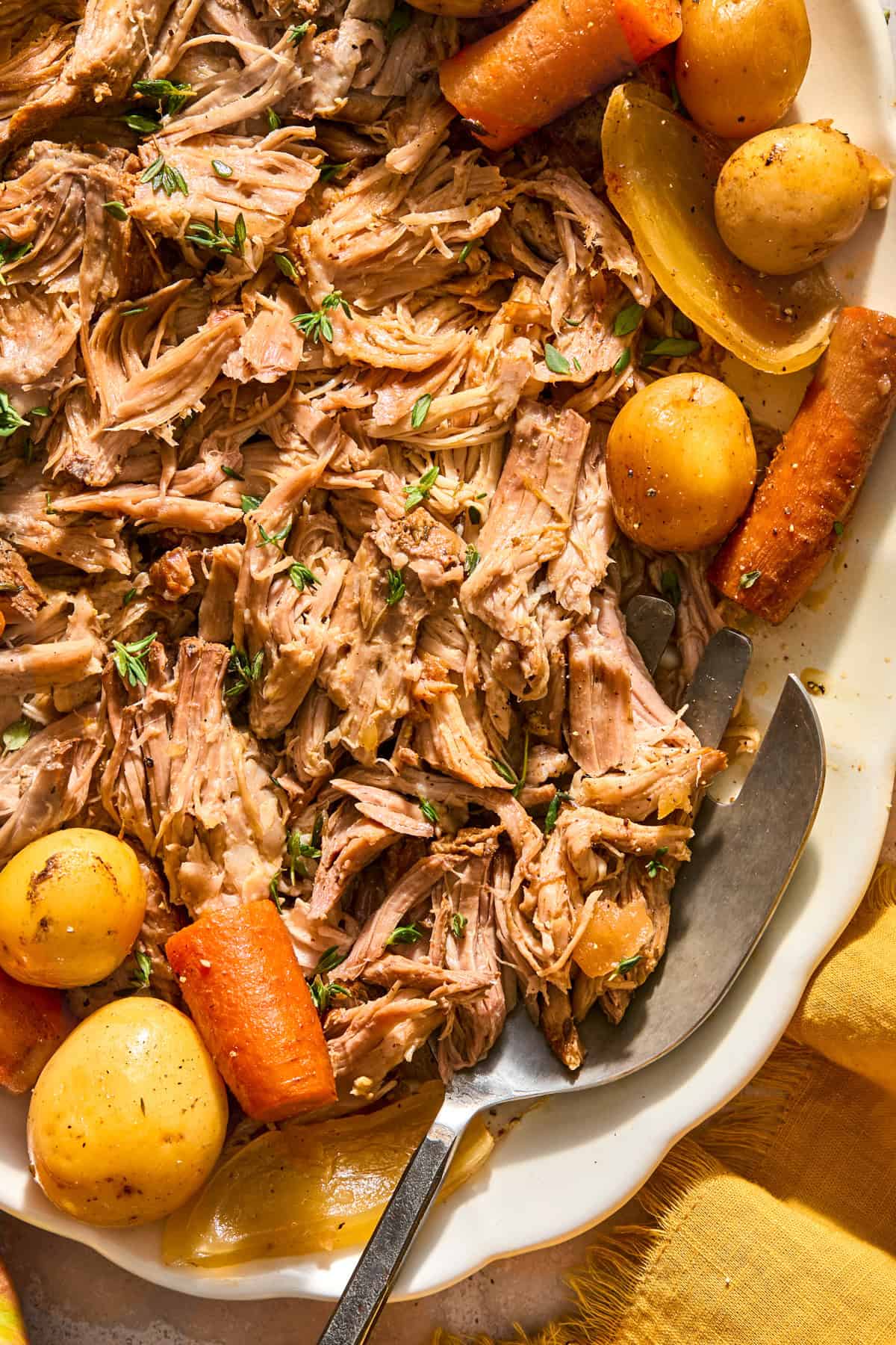 Pulled pork roast on plate with carrots and potatoes.