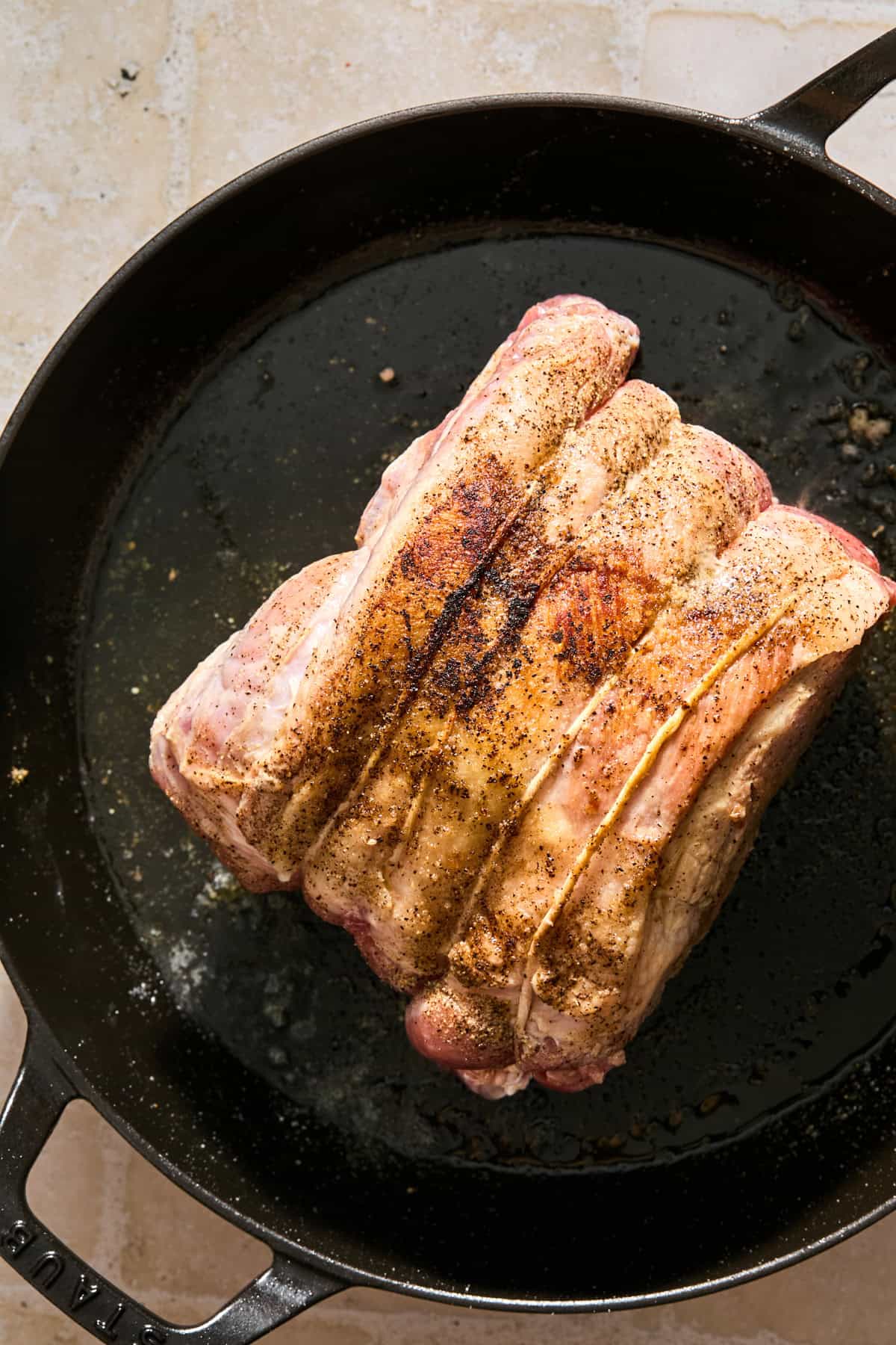 Seared pork shoulder in skillet with oil.