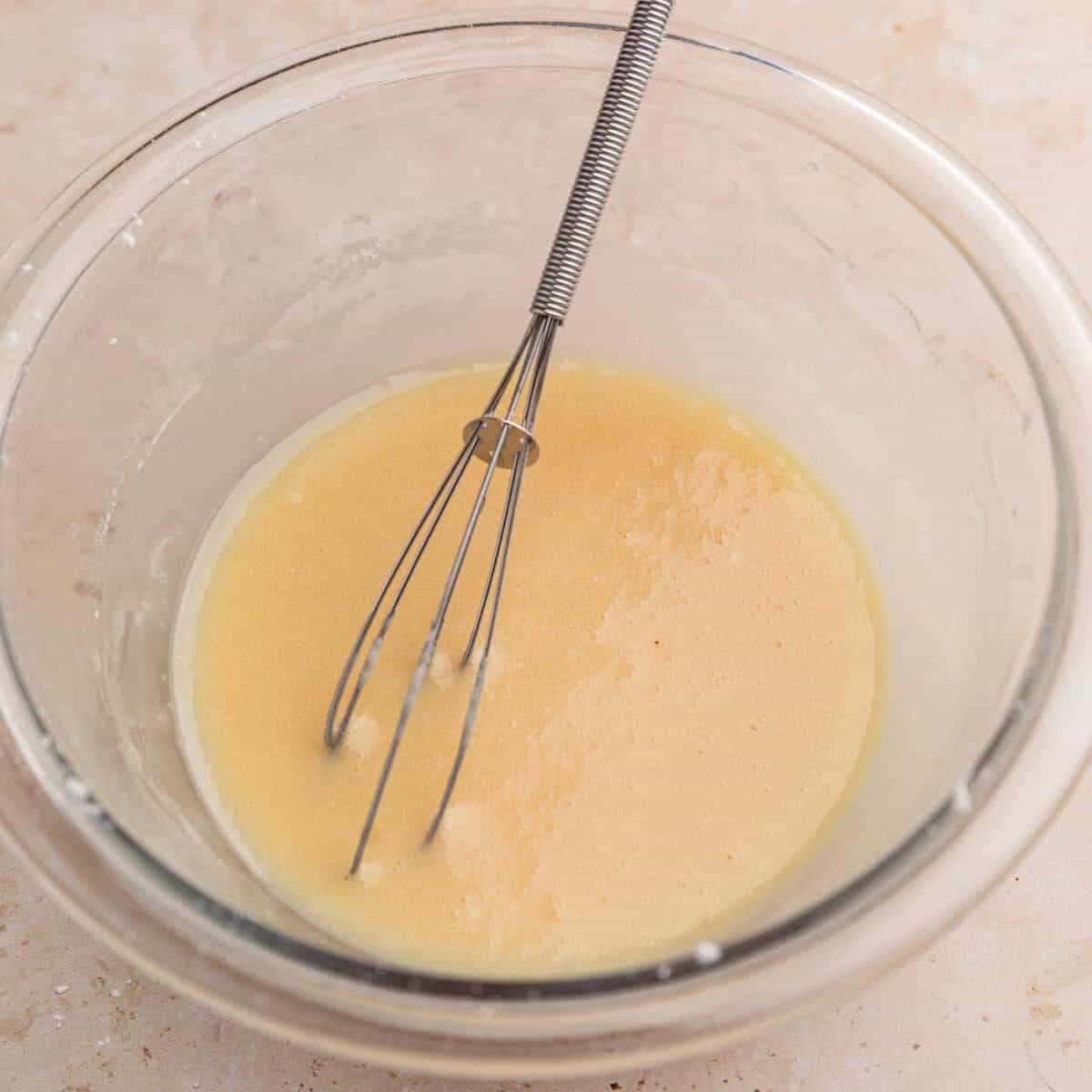 Apple cider glaze in bowl with whisk.