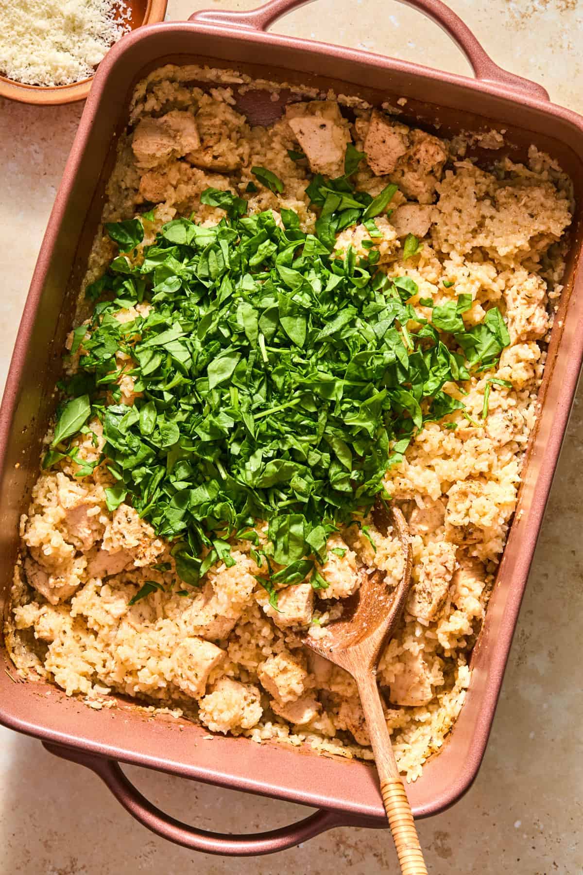 Chopped spinach added to baking pan with rice and chicken.