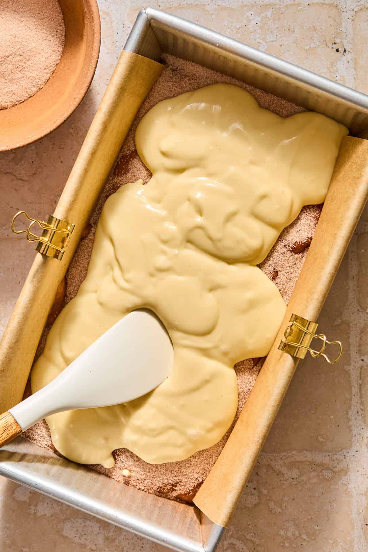 Cream cheese layer spread over top of cinnamon and sugar layer in bread pan.
