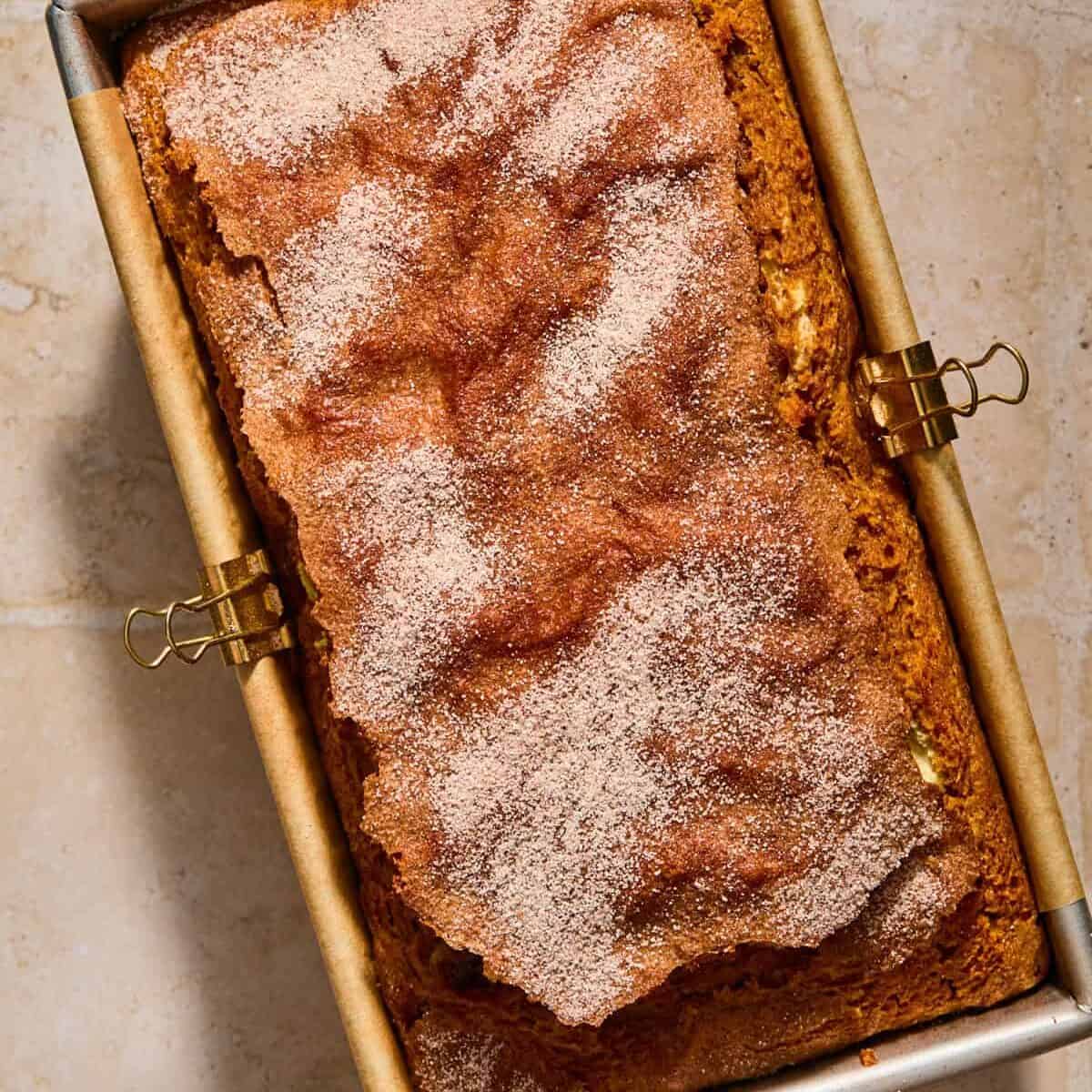 Baked pumpkin bread in pan topped with cinnamon and sugar.