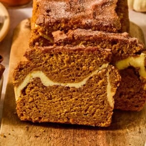 Pumpkin bread sliced on cutting board with cream cheese and cinnamon swirl in center.