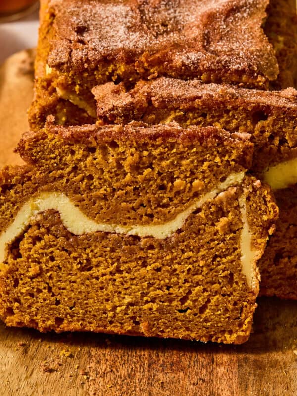 Pumpkin bread sliced on cutting board with cream cheese and cinnamon swirl in center.