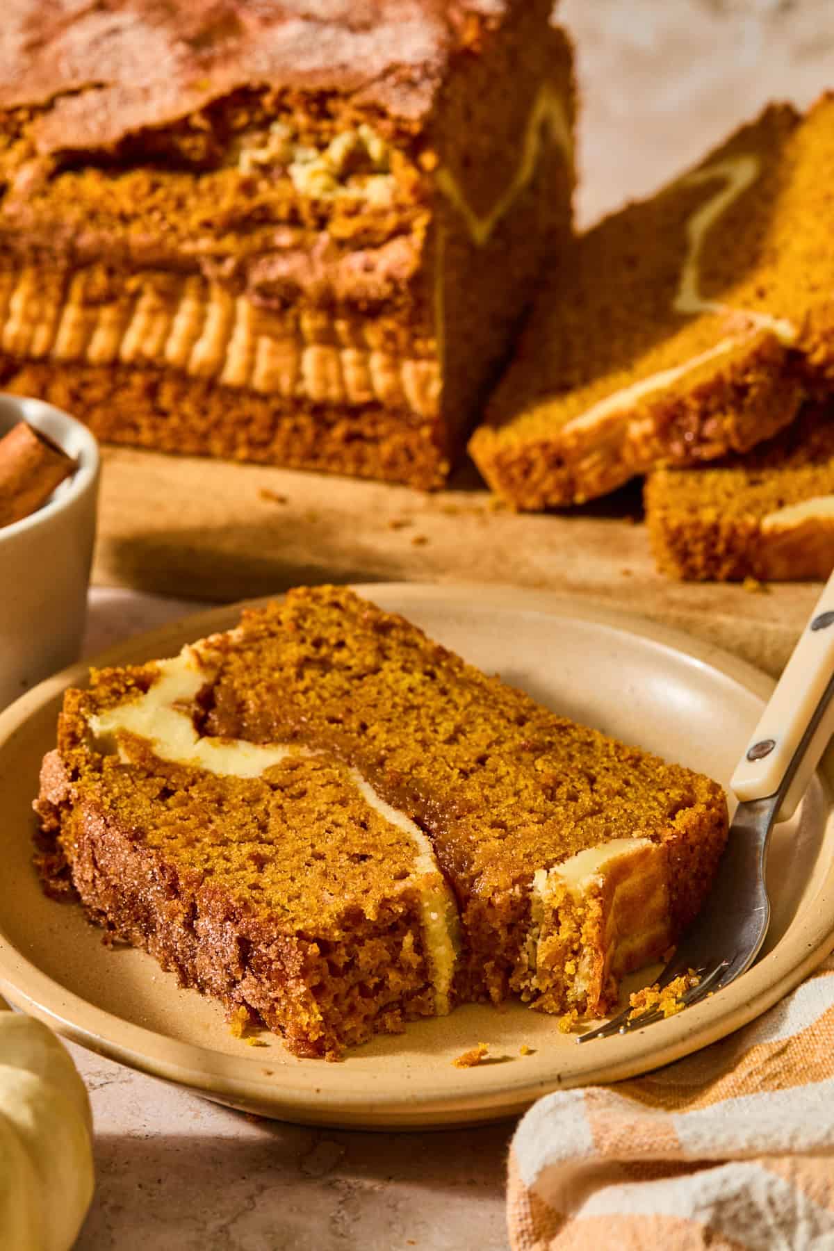 Slice of pumpkin bread with a cream cheese and cinnamon sugar layer on plate.