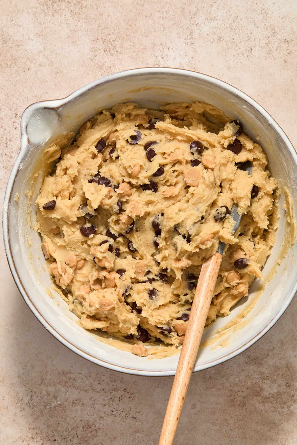 Peanut butter chips and chocolate chips mixed into cookie dough with spatula.