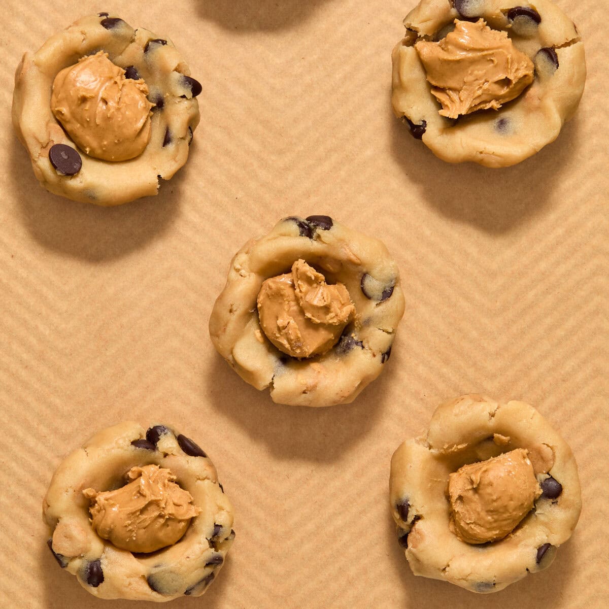 Peanut butter dollops in cookie dough balls on pan.