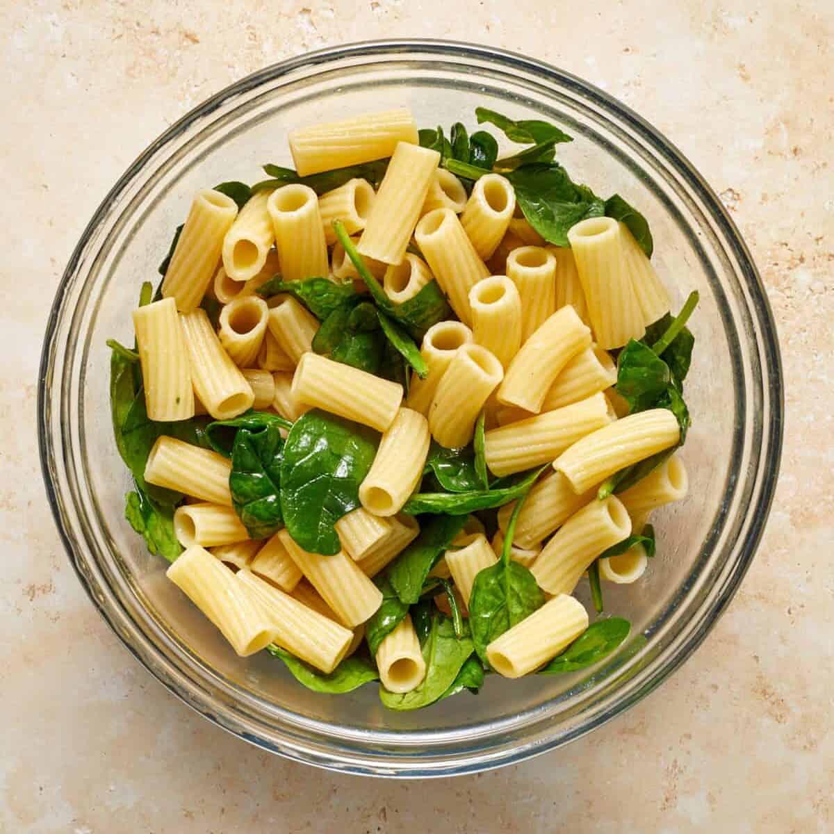 Rigatoni and spinach in glass mixing bowl.