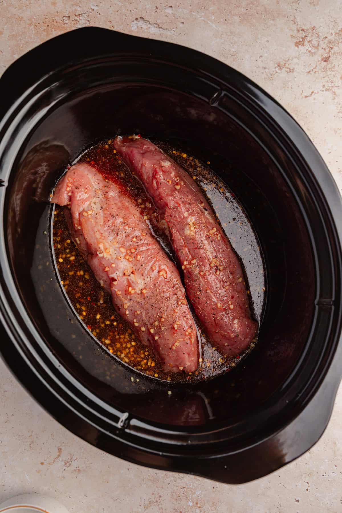 Crockpot with pork tenderloins and sauce before cooking.