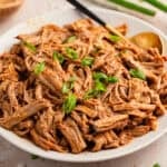 Pulled honey garlic pork tenderloin on plate with serving utensils.
