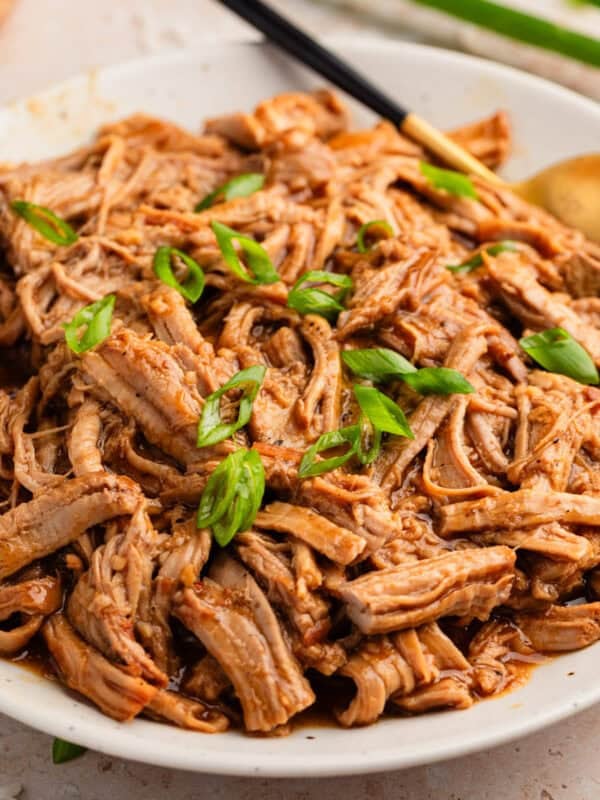 Pulled honey garlic pork tenderloin on plate with serving utensils.