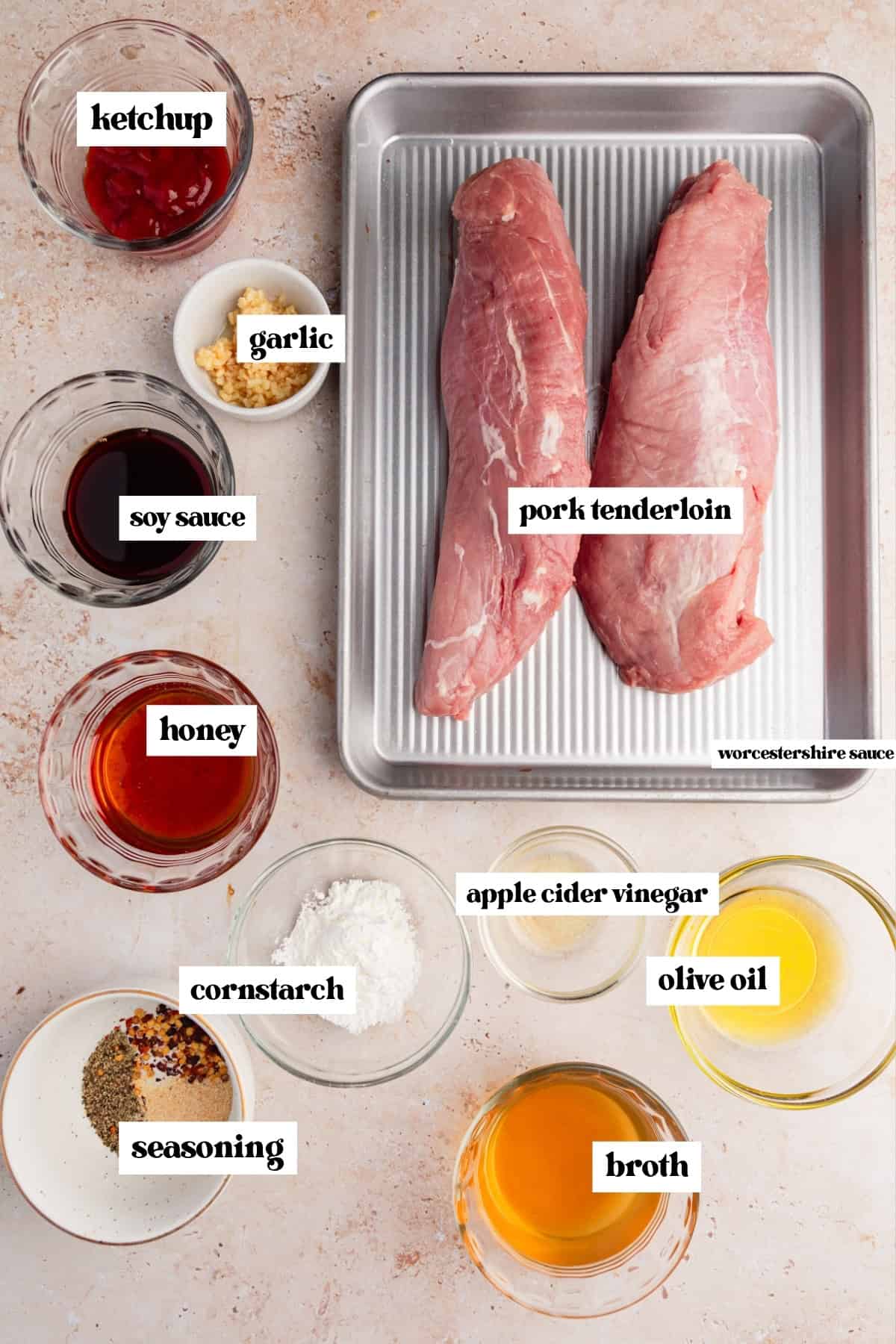 Raw pork tenderloin, ketchup, soy sauce and other labeled ingredients on surface.