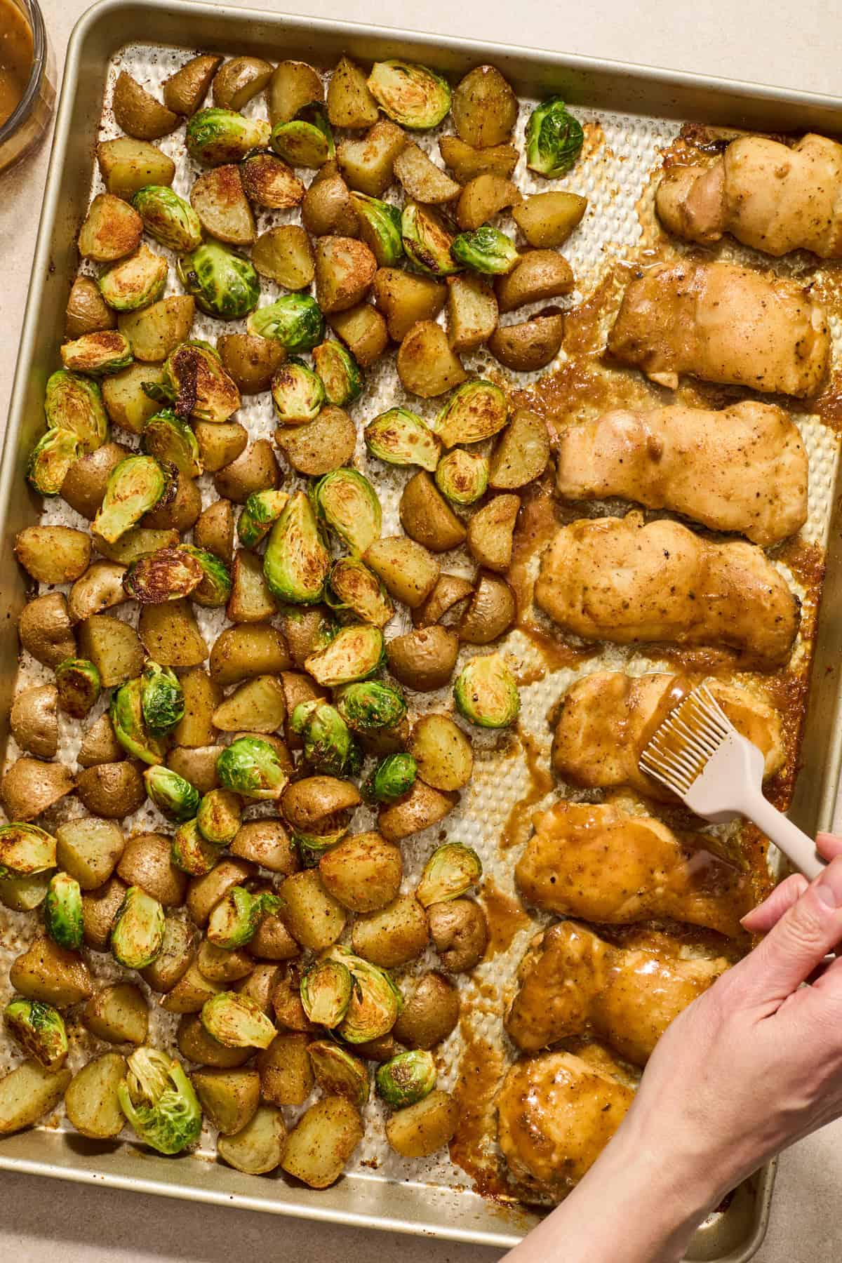 Honey mustard sauce being brushed onto chicken on sheet pan.