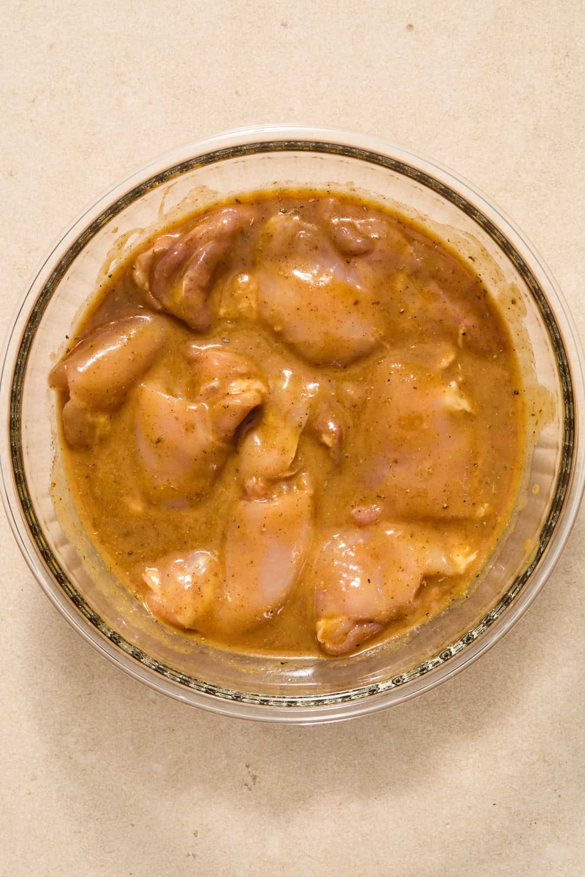 Chicken thighs marinating in glass bowl.