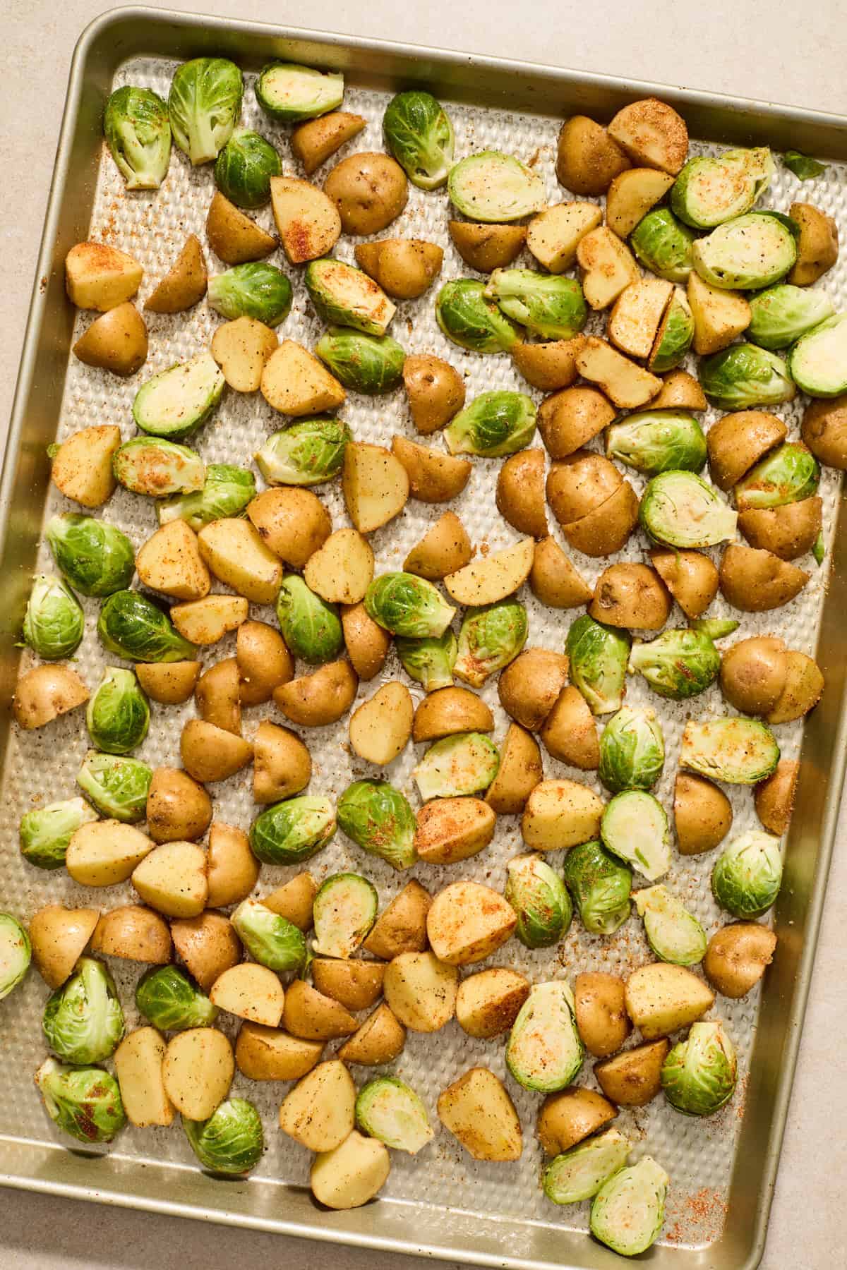 Potatoes and Brussels sprouts seasoned on sheet pan before cooking.