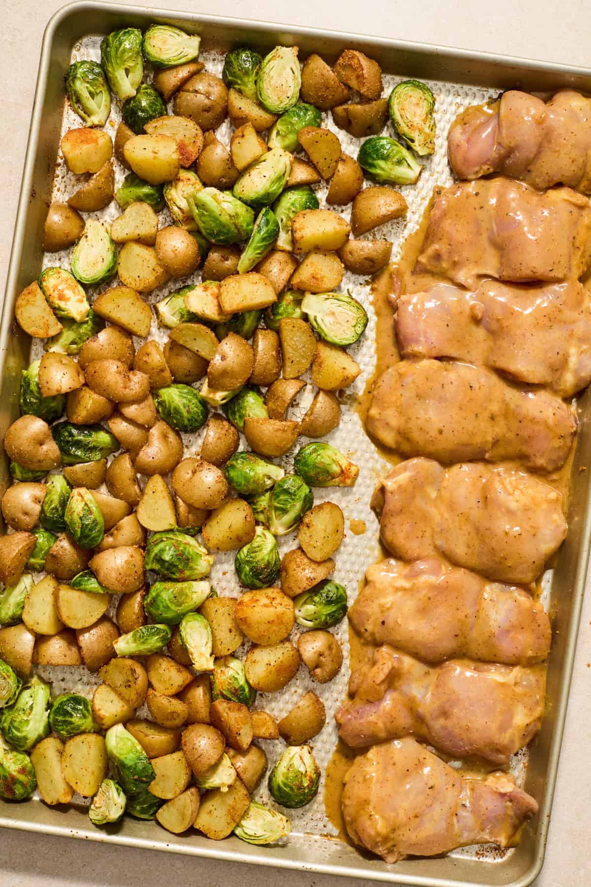 Honey mustard chicken added to sheet pan with potatoes and vegetables.