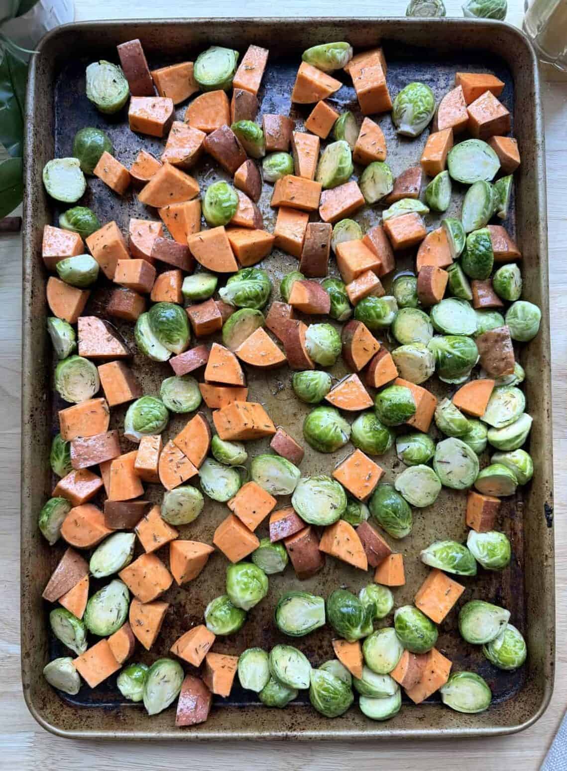 Sheet pan with sweet potatoes and brussels sprouts before roasting.