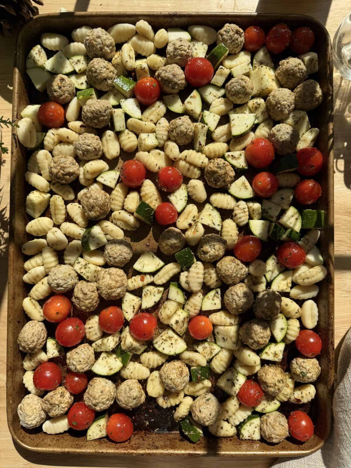 Sheet pan with gnocchi, frozen meatballs, tomatoes and other ingredients.