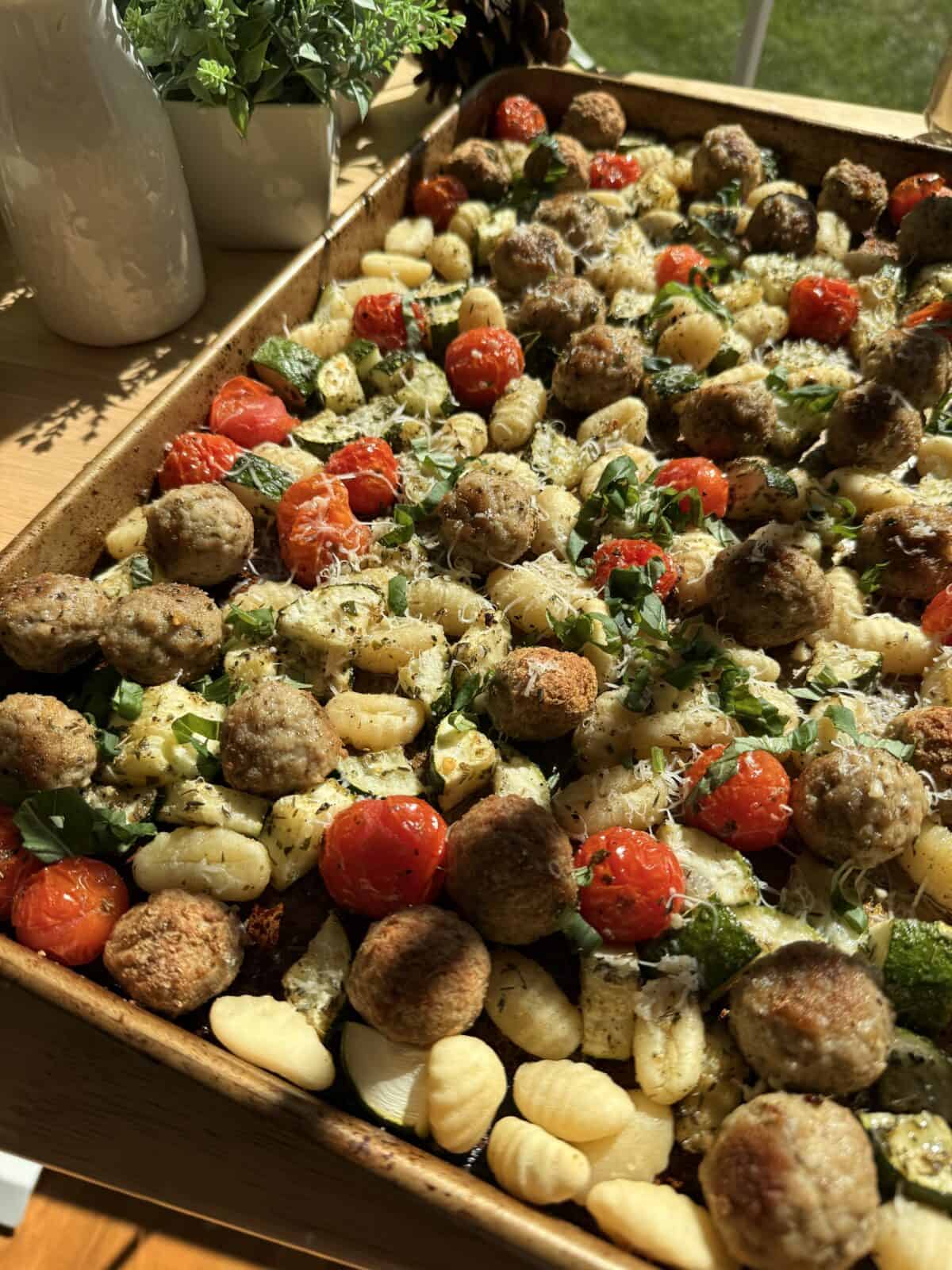 Garnished meatballs and gnocchi on pan with parmesan and basil.