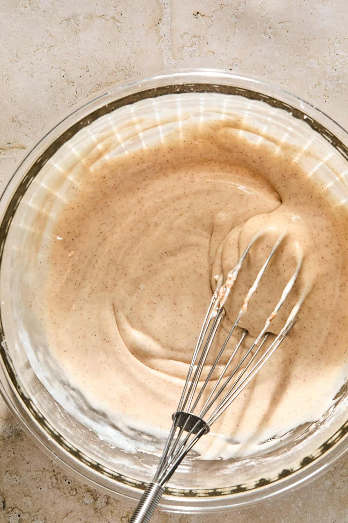 Cinnamon icing glaze in bowl with whisk.