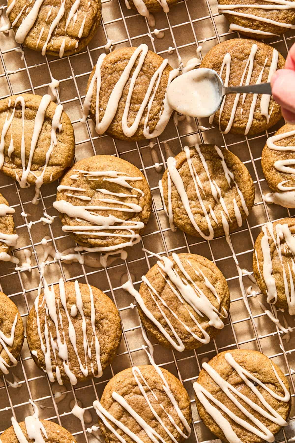 Icing being drizzled over cookies on cooling rack.