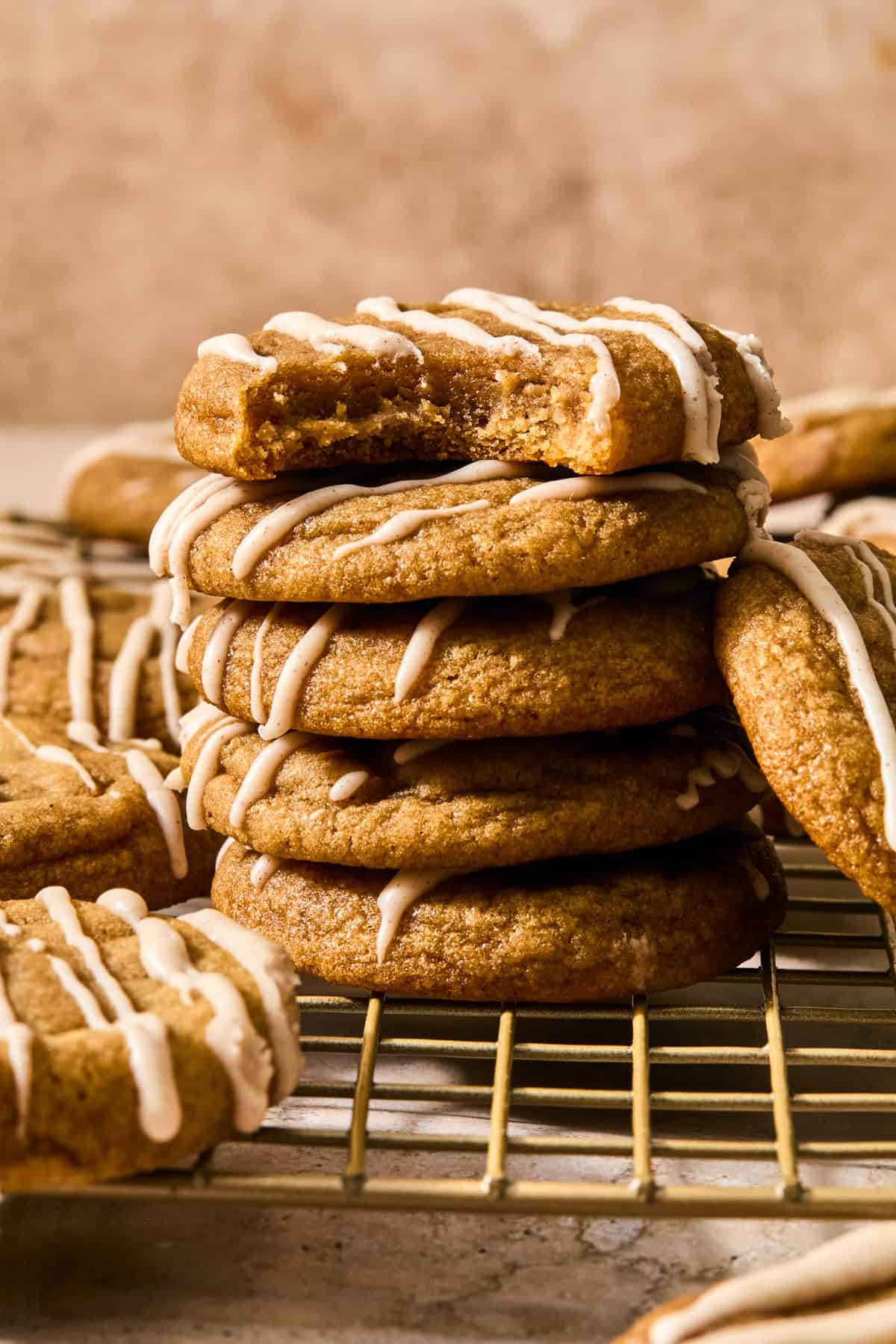Stack of maple and brown sugar cookies with cinnamon icing drizzle and bite taken out of top cookie.