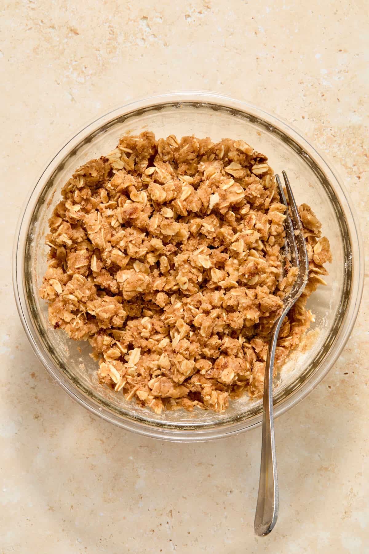 Crisp oat topping mixture in glass bowl with fork.