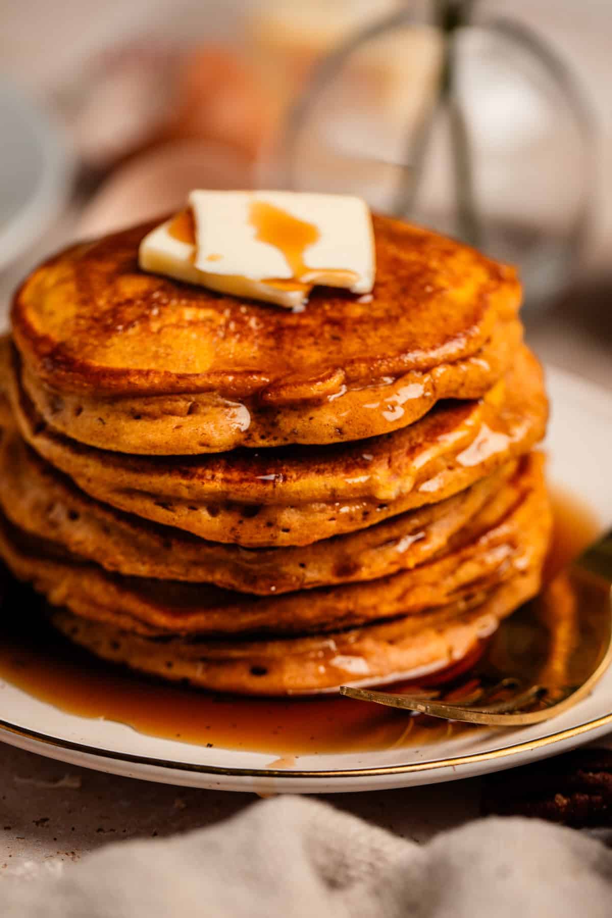 Stack of pancakes on plate with butter and maple syrup on top.