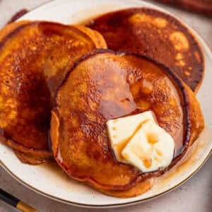 Pumpkin ricotta pancakes on plate with butter and syrup.