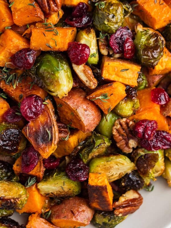 Roasted brussels sprouts and sweet potatoes on plate with pecans and cranberries.