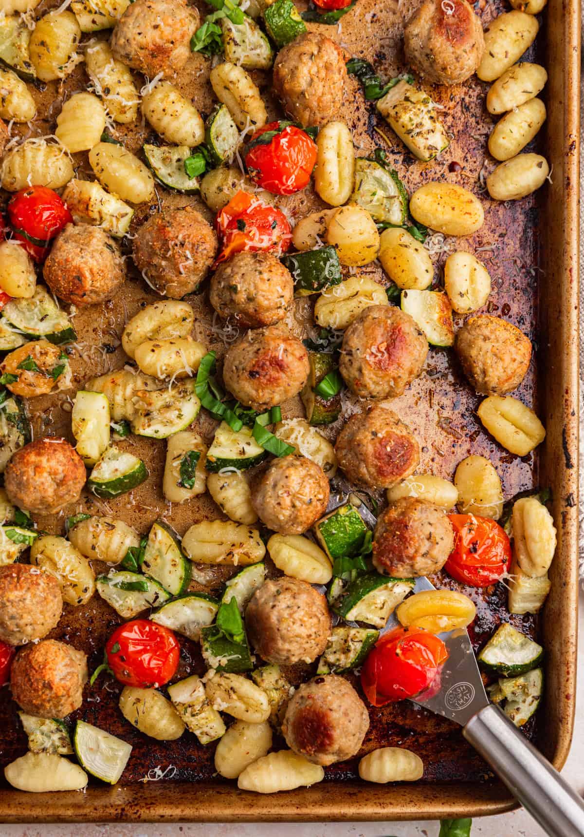 Sheet pan with spatula scooping up meatballs, vegetables and other ingredients.
