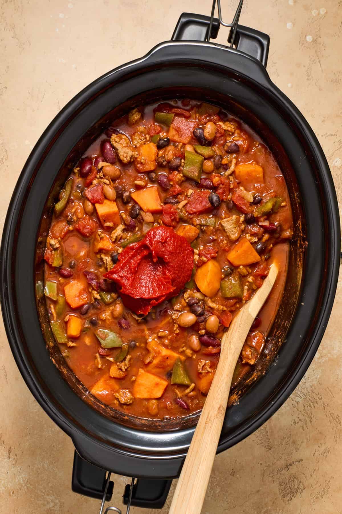 Sweet potato turkey chili with tomato paste added in and spoon propped.