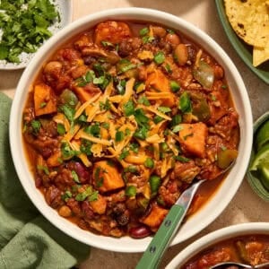 Bowl of turkey and sweet potato chili topped with cheese and other ingredients.