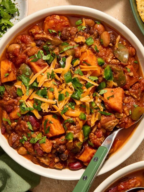 Bowl of turkey and sweet potato chili topped with cheese and other ingredients.
